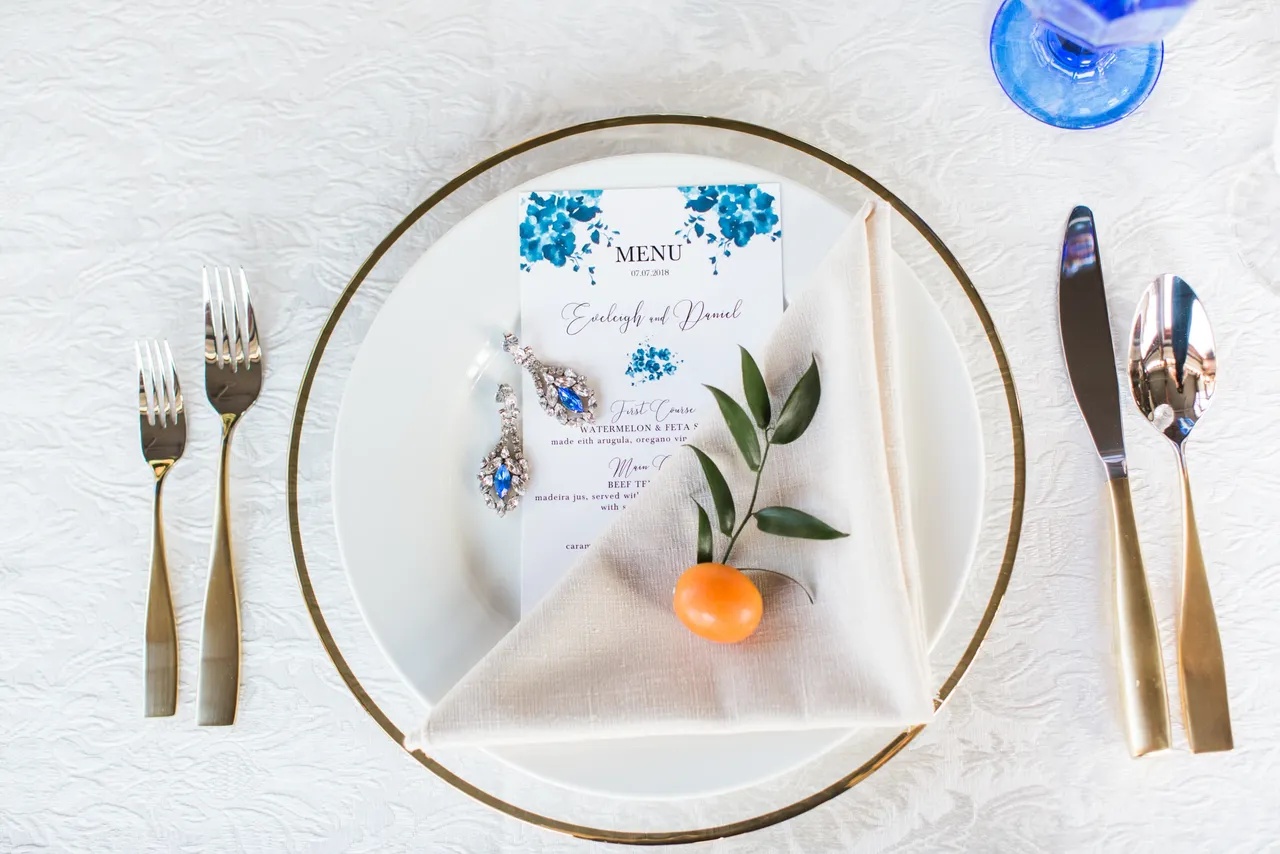 Place setting detail — menu card, jewellery, and gold flatware.